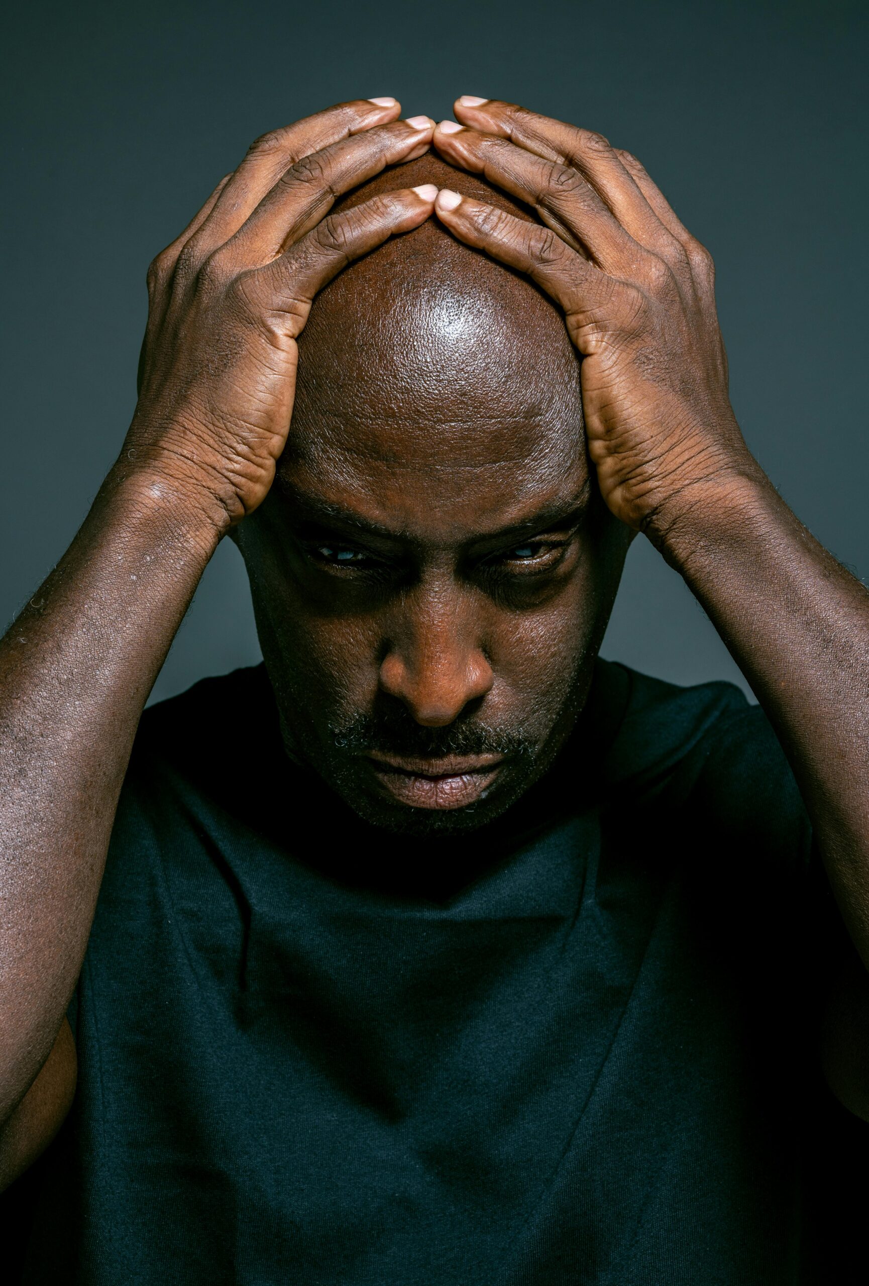 Man in blue crew neck shirt holding his head with both hands